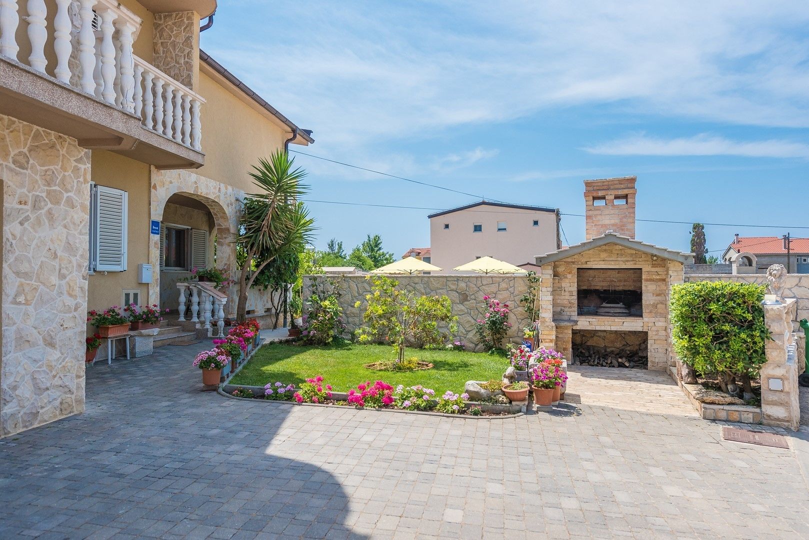Ein Innenhof mit einem Steinhaus, ein kleiner Garten mit Blumen und einem Grillplatz.