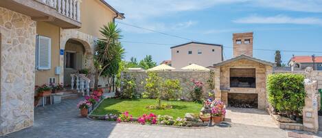 A courtyard with a stone building, a small garden with flowers, and a barbecue area.