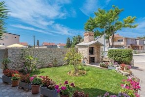 A stone-built outdoor kitchen with a chimney, surrounded by a well-maintained garden with various flowering plants and a lawn.