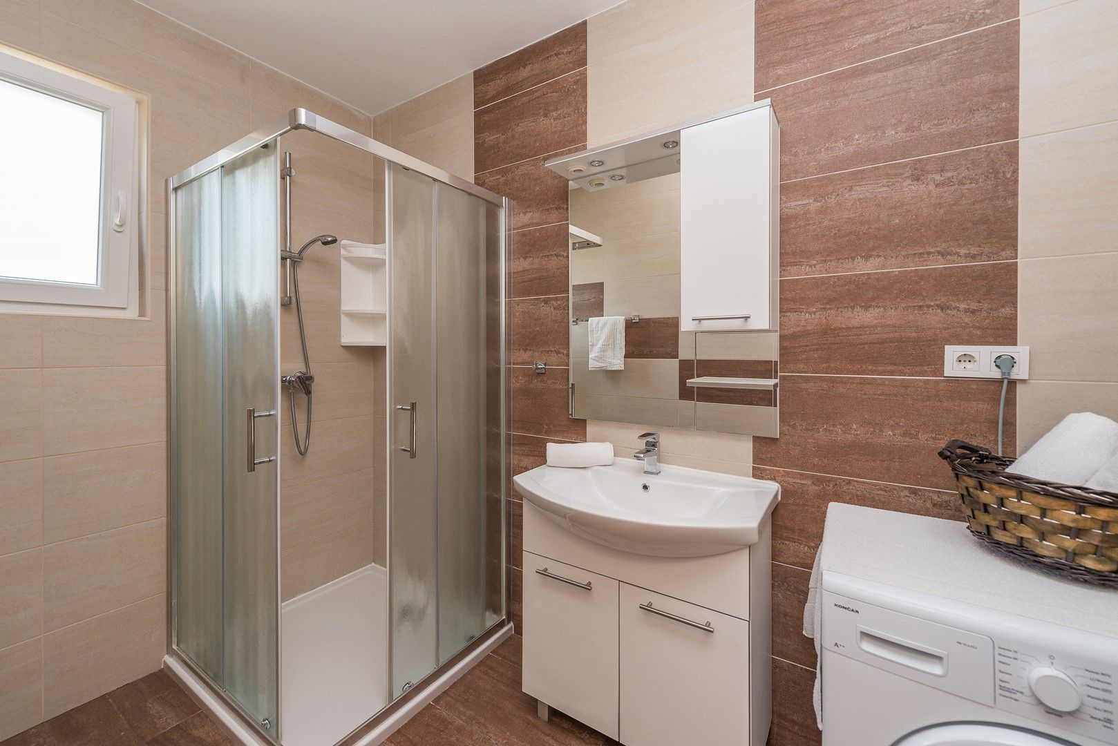 A modern bathroom with a glass-enclosed shower, a white sink, a mirror, and a washing machine.