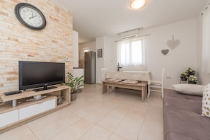 A modern living room with a flat-screen TV, a brick accent wall, a dining area with a table and chairs, and a sofa.