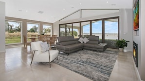 Amplia sala de estar con un sofá modular grande, comedor con sillas de madera y vista a la playa a través de amplios ventanales.