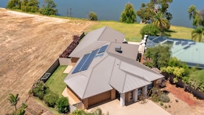 Una casa de dos pisos con techo inclinado, paneles solares y un patio grande con piscina.