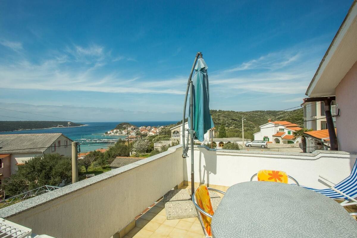 Un balcón con vistas al mar, una silla y una mesa.