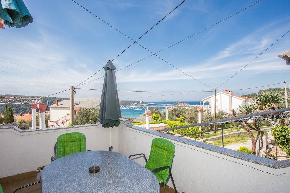 Un balcón con mesa y sillas, con vistas a la costa, casas y un puente.