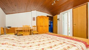 A bedroom with a wooden ceiling, a bed with a floral bedspread, a wooden desk with chairs, and a wardrobe. - Apartments Antonija (Rab)