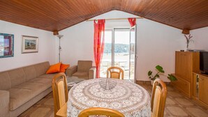 A cozy living room with a wooden ceiling, a sofa with orange cushions, a round table with a lace tablecloth, and a TV on a wooden cabinet. - Apartments Antonija (Rab)