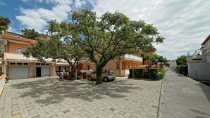 A paved courtyard with a tree, parked cars, and buildings with balconies. - Apartments Marica 3131 (Rab)