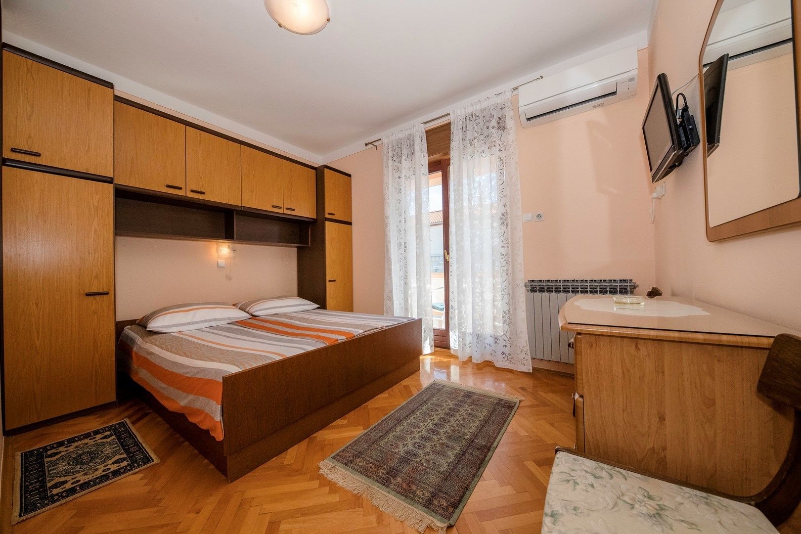 Une chambre à coucher de taille réduite, comprenant un lit, une armoire en bois, une petite salle de bain avec un lavabo et un miroir.