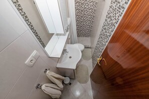 A bathroom with a white sink, a mirror, and a toilet. There are two towels on the floor.