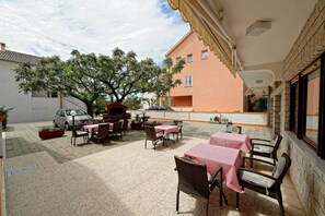 An outdoor patio area with tables and chairs, a tree, and a building in the background.