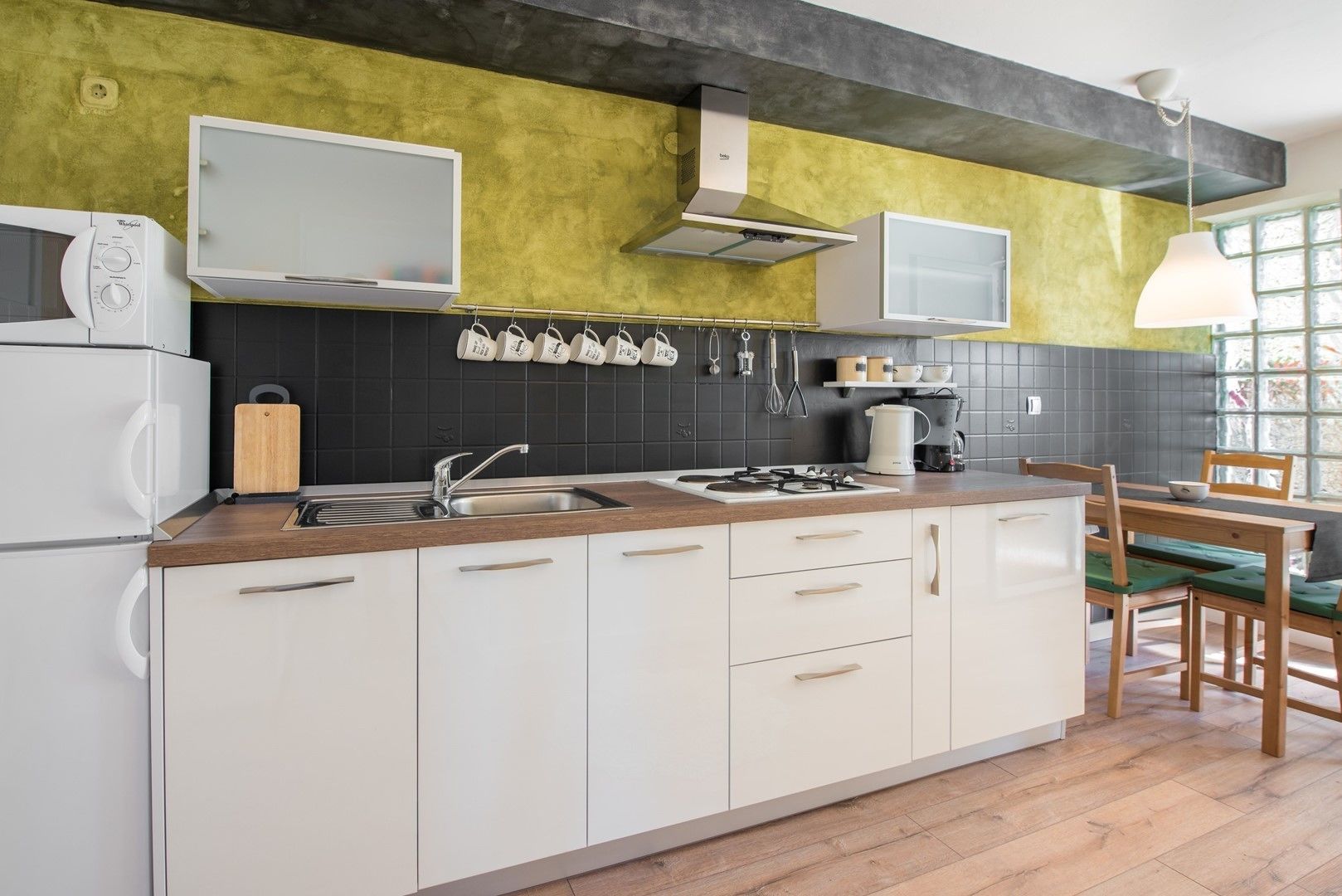 Een moderne keuken met witte kasten, een houten aanrecht, een gasfornuis en een spoelbak. Er is een raam met uitzicht op groen.