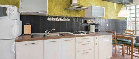 Een moderne keuken met witte kasten, een houten aanrecht, een gasfornuis en een spoelbak. Er is een raam met uitzicht op groen.