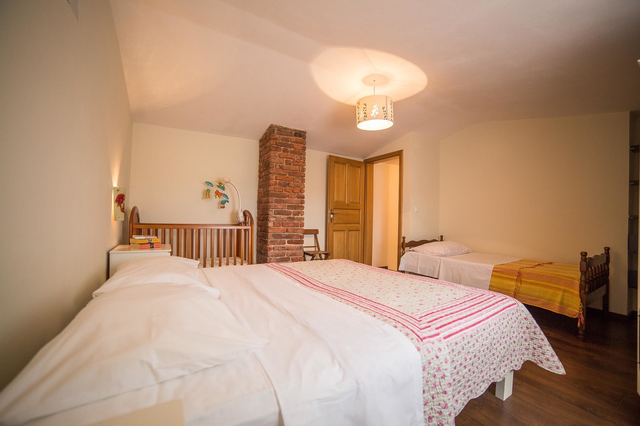 A bedroom with two beds, a brick wall, wooden furniture, and a ceiling light fixture.