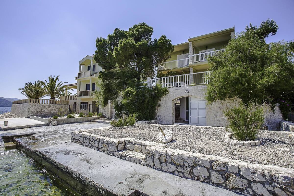 A coastal hotel with a stone facade, multiple balconies, and a view of the sea.