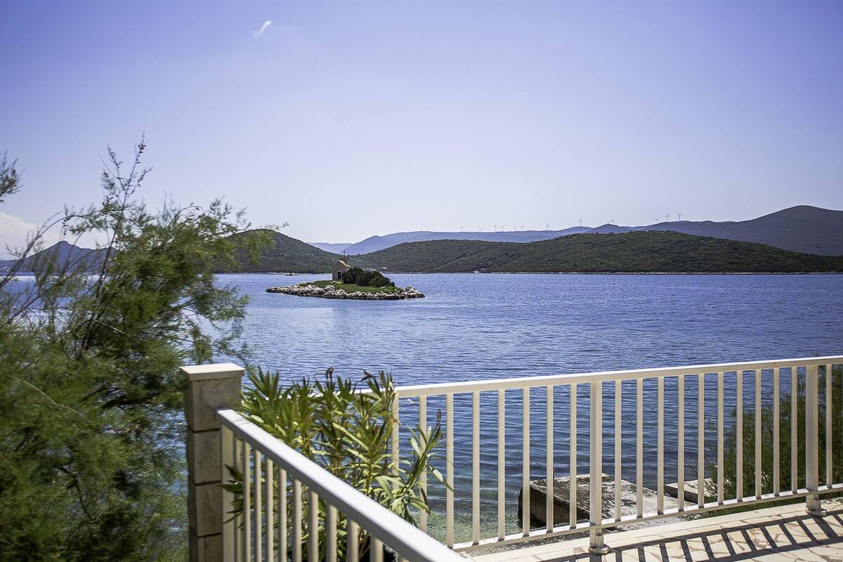 A view of a lake with a small island, a distant mountain range, and a clear sky.
