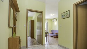 A hallway with a wooden cabinet, a mirror, and a door leading to a living area with a sofa and a map on the wall. - Apartments Krstičević (Slivno)