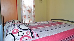 Ein Schlafzimmer mit einem Bett, einem Fenster mit blumigen Vorhängen und einer Tür.