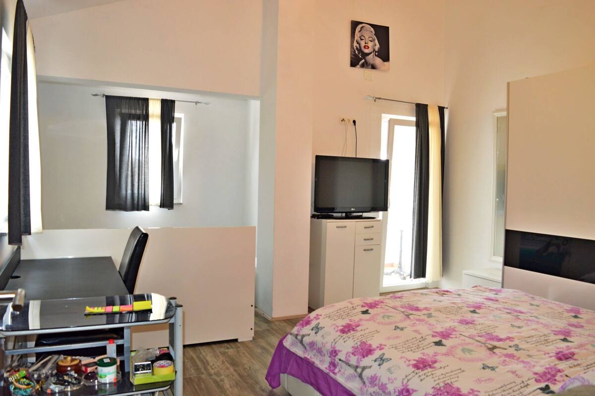 A hotel room with a bed, a desk with a chair, a television, and a wardrobe.