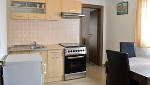 A compact kitchen with a stove, sink, and cabinets. There is a dining table with chairs. - Apartments Ante Seline (Starigrad)