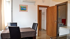 A dining area with a table and chairs, a coat rack, and a kitchen area with a sink and a refrigerator. - Apartments Ante Seline (Starigrad)