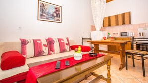 A cozy living room with a sofa, a wooden table, and a kitchen area in the background. - Apartments Divna Tomas (Omis)