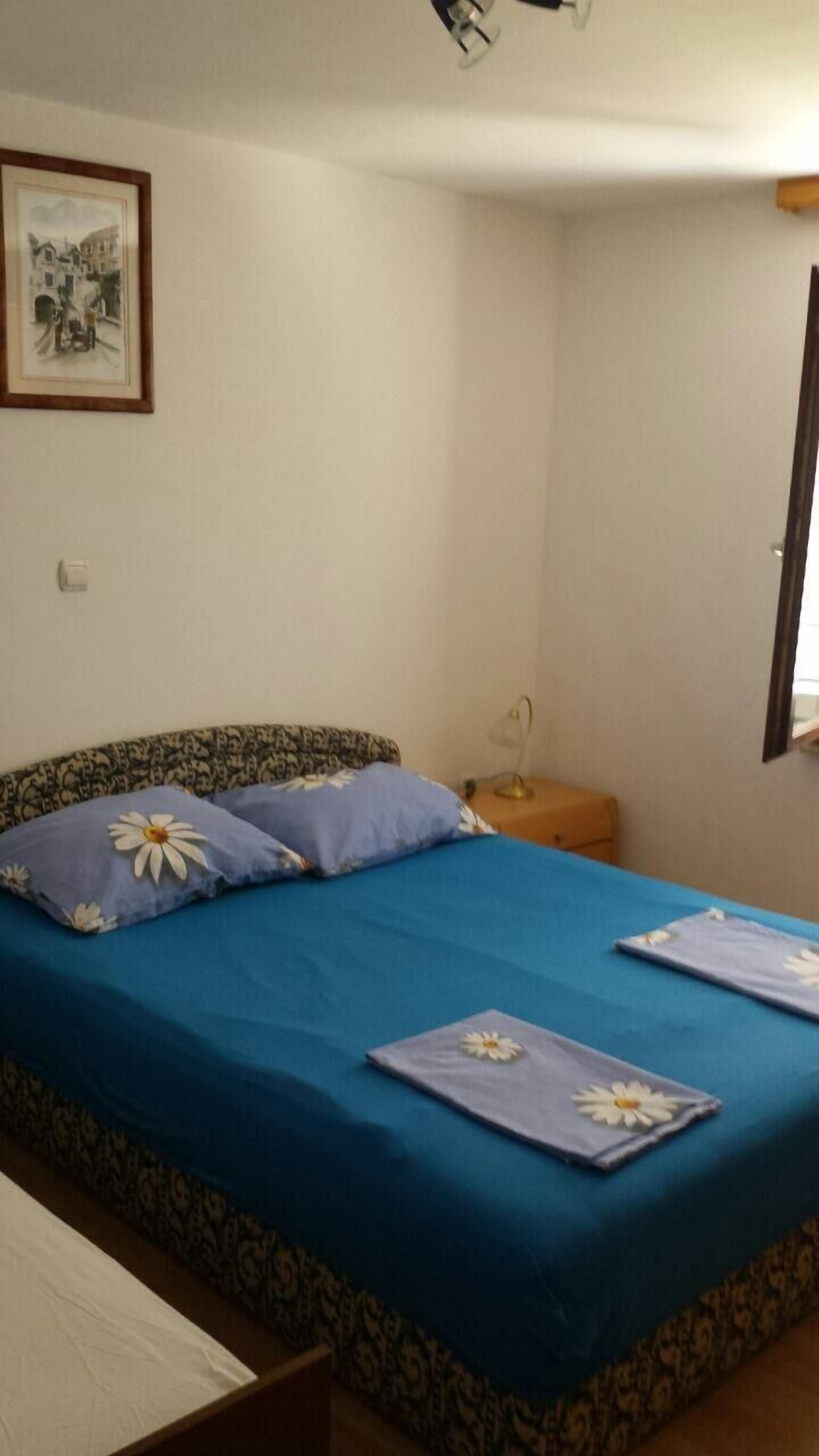 A bedroom with a bed, a nightstand, a framed picture on the wall, and a window.