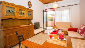 A cozy living room with a wooden cabinet, a TV, a sofa, and a dining area with a table and chairs. - Apartments Divna Tomas (Omis)