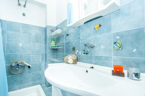 A bathroom with a white sink, blue tiles, a towel rack, a soap dish, and a shower head. - Apartments Divna Tomas (Omis)