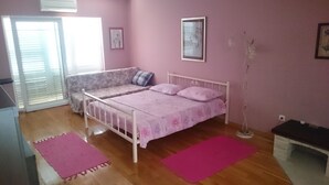 Ein Schlafzimmer mit Bett, einer Couch, einem Fenster mit Jalousien, einem Bild an der Wand und einer Stehlampe.