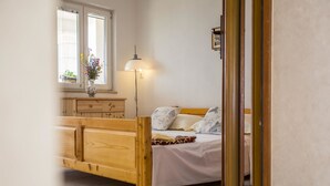 A wooden bed with white bedding, a bedside lamp, a window with a view, and a wooden dresser. - Holiday House Domina (Postira)
