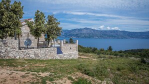 A stone building with a satellite dish, surrounded by trees and overlooking a lake with mountains in the background. - Holiday House Domina (Postira)
