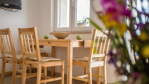 A dining area with wooden chairs and a table, a television mounted on the wall, and a window with a view of the outside. - Holiday House Domina (Postira)
