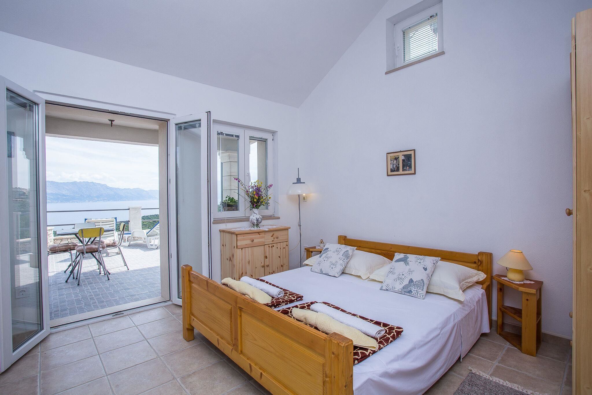 A bedroom with a wooden bed, a nightstand, a lamp, a dresser, and a view of the outdoors through a sliding door.