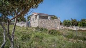 A stone house with a red-tiled roof, surrounded by greenery and a clear blue sky. - Holiday House Domina (Postira)