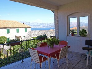 A balcony with a table and chairs, a view of the sea and mountains, and a stone building in the background. - Apartments Janja Postira (Postira)