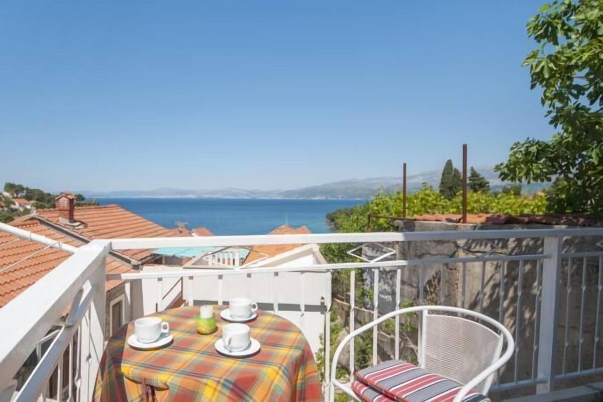 A balcony with a table set for two, overlooking a coastal view.