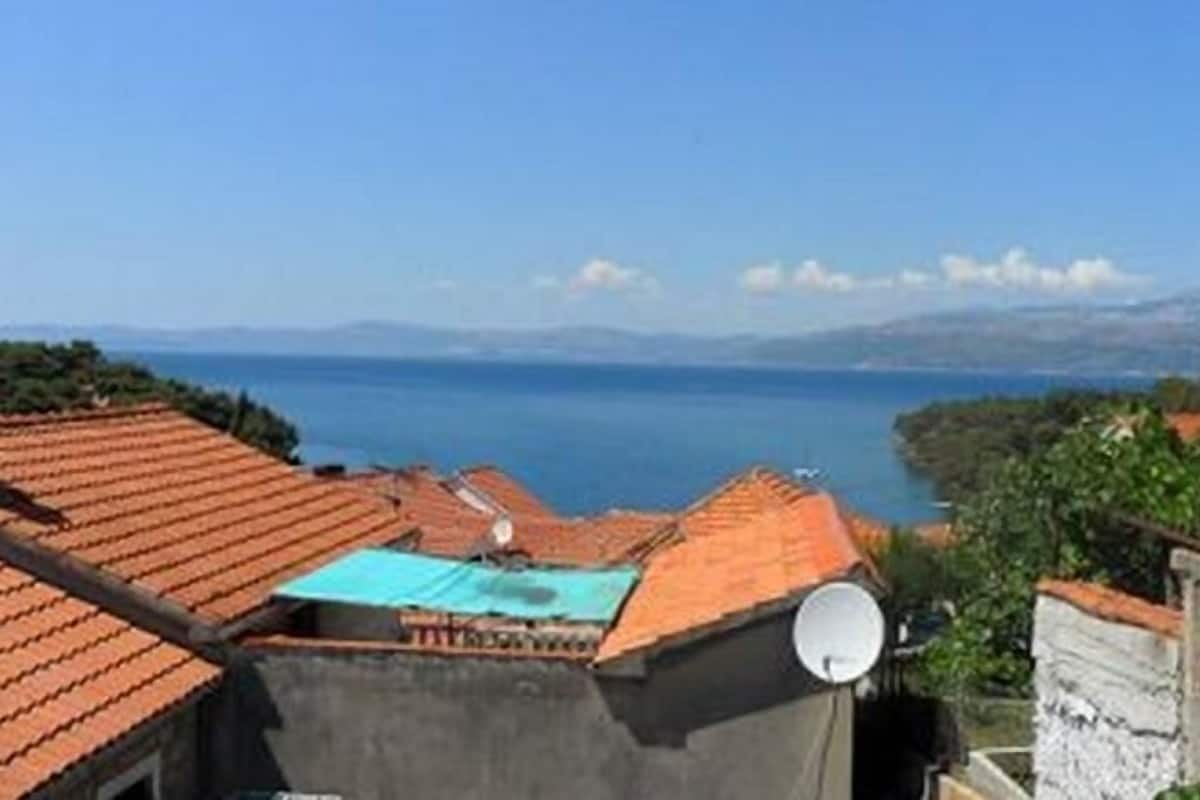 A coastal view with terracotta-roofed buildings, a satellite dish, and a clear blue sky.