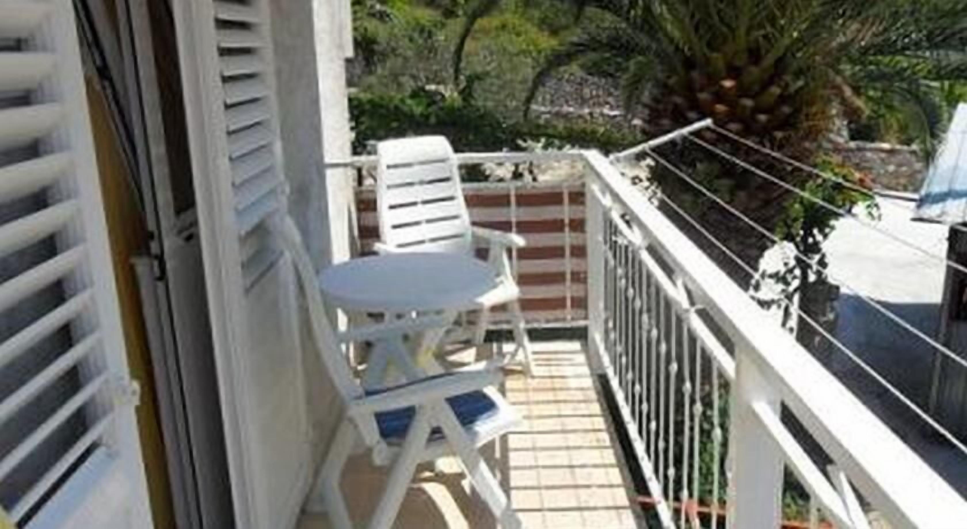 A balcony with a white table and chairs, a small potted plant, and a view of a tree and building in the background.