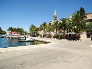 A waterfront area with a marina, palm trees, and a historic building with a tower. - Apartments Vila Marija (Supetar)