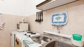 A compact kitchen with a stove, sink, and a small countertop. - Apartments Blaženka (Omis)