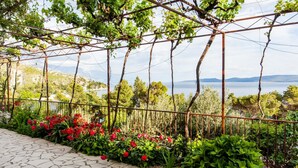 A garden with a pergola, red flowers, and a view of a lake. - Apartments Blaženka (Omis)