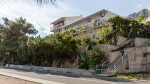A building with a stone staircase leading to a balcony, surrounded by greenery and a clear sky. - Apartments Blaženka (Omis)