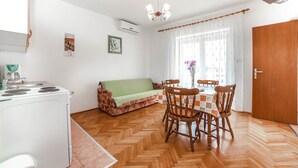 A compact kitchen with a stove, a sofa, and a dining table with chairs. There is a window with curtains and a door to the right. - Apartments Jasko / Two Bedroom Jasko 2 (Rab)