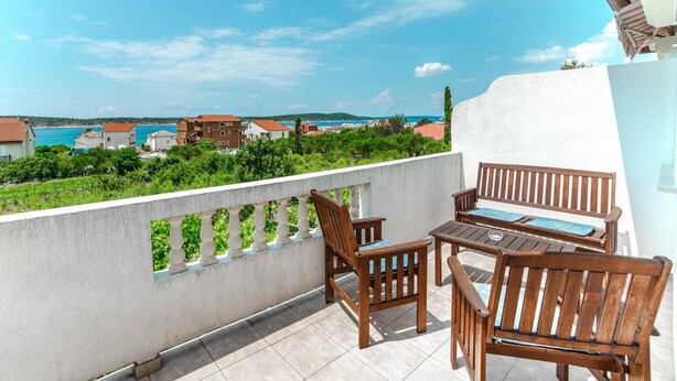 A balcony with wooden furniture and a view of the sea and buildings. - Apartments Jasko / Two Bedroom Jasko 2 (Rab)