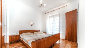 A bedroom with a wooden bed, a nightstand, a wooden wardrobe, and a window with sheer curtains. - Apartments Jasko / Two Bedroom Jasko 2 (Rab)