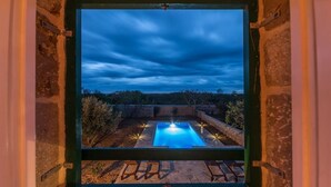 Vista de una piscina al anochecer, con un solárium de piedra y bancos.