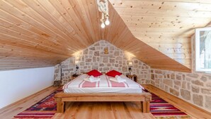 Un dormitorio acogedor en el ático, con pared de piedra, techo de madera y cama con almohadas rojas.