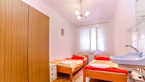 Una camera da letto con due letti singoli, un armadio in legno, un bagno con lavandino e una finestra con tende leggere.