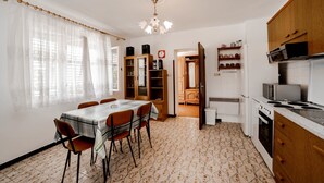 Zona pranzo con tavolo e sedie, cucina con pensili ed elettrodomestici, e pavimento decorato.